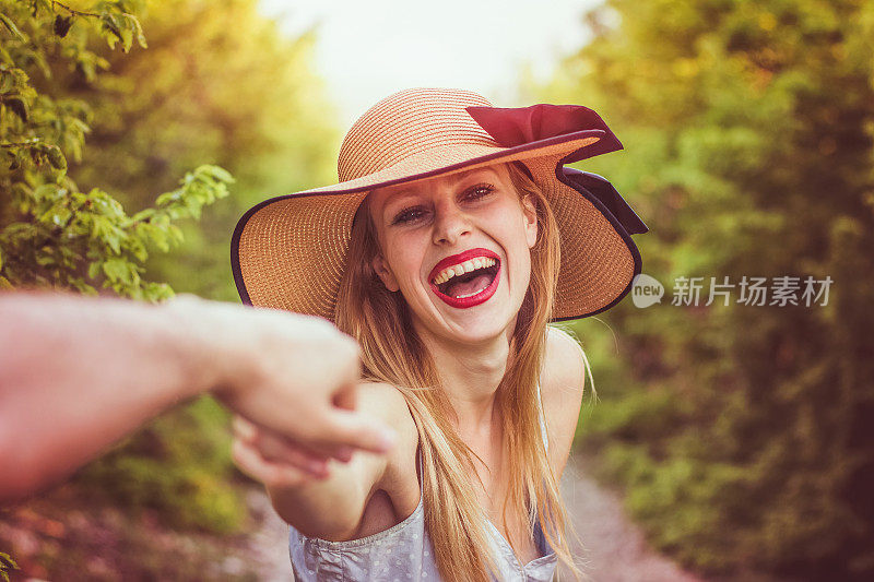 美丽微笑的女人戴着一顶帽子牵着男朋友的手在一个美丽的晴天在森林里