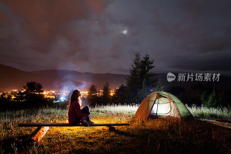 沉思的女孩坐在帐篷和篝火旁的长椅上