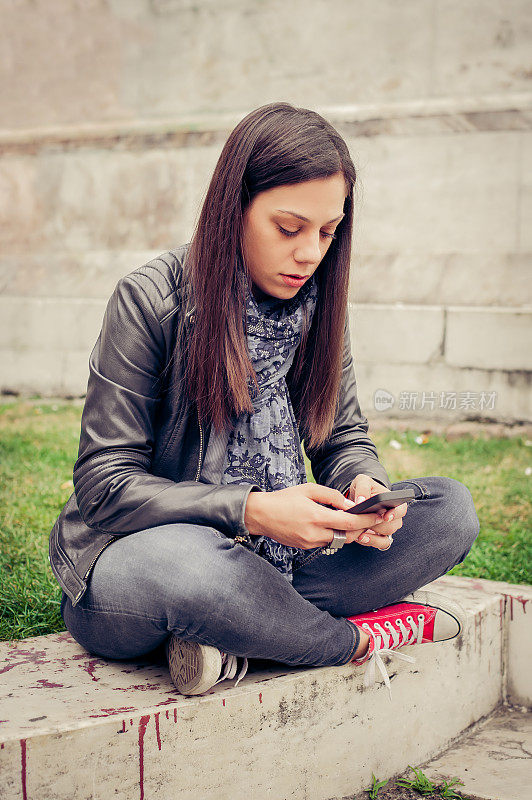 一个女人坐在城市街道上，发信息，用智能手机聊天