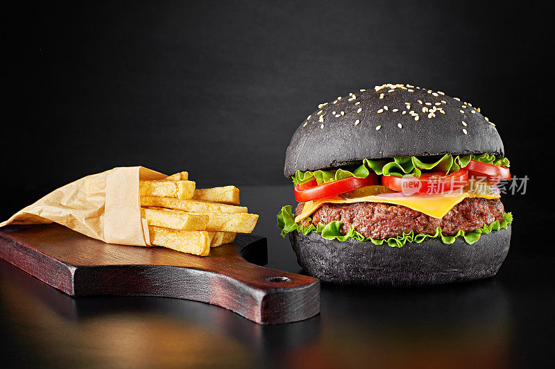 黑色汉堡和薯条放在木头砧板上，以黑色为背景。