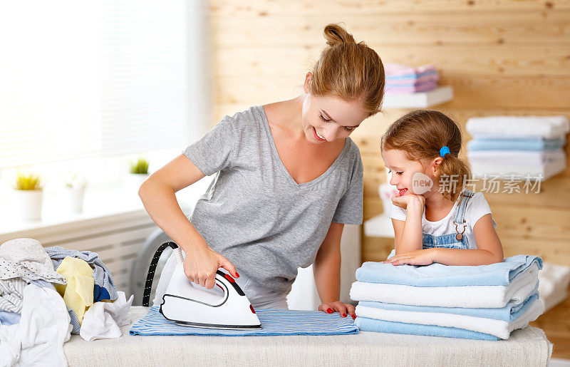 幸福的家庭，母亲，家庭主妇和孩子女儿在洗衣熨烫衣服