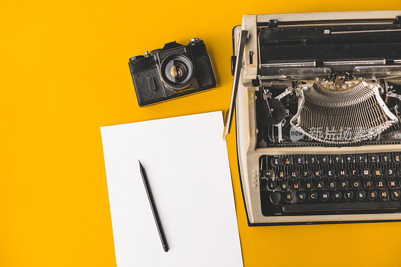 旧打字机，老式胶卷相机，一张纸和一支铅笔在黄色的背景，顶视图。创造性的概念