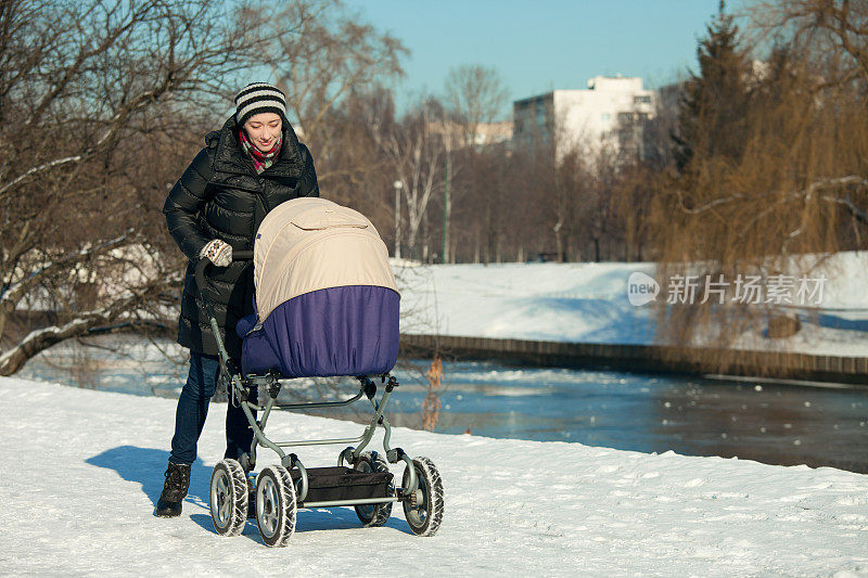 一个女人推着婴儿车在冬天的公园散步