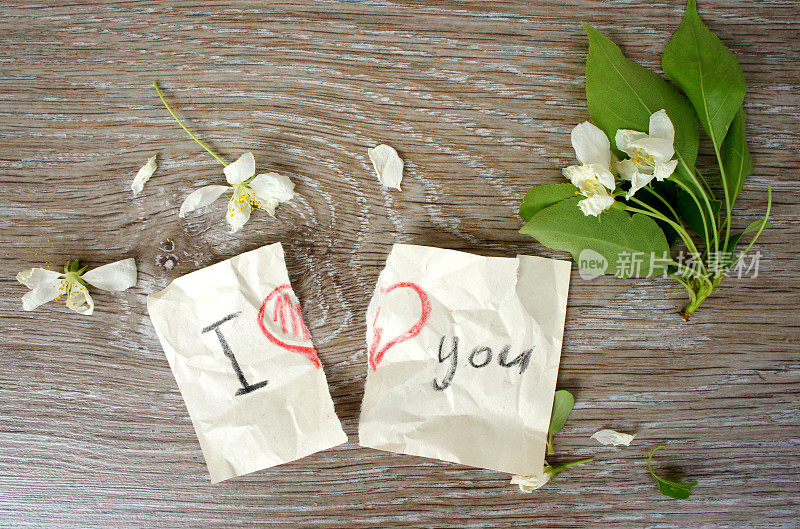 “我爱你”这句话里的心被撕成两半。破碎的笔记在纸上用铅笔，木制的背景上有花苹果树。平的。