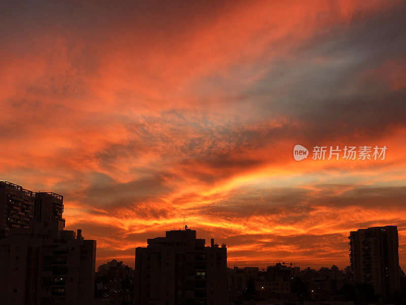 日落在城市与令人惊叹的彩色魔术云彩。春天的天空与红云和屋顶的看法。