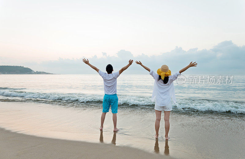 一对夫妇站在沙滩上，举起手臂