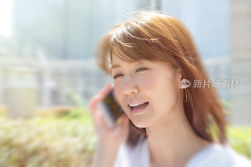 年轻的亚洲女子使用智能手机在一个美丽的阳光明媚的日子走在城市里的特写