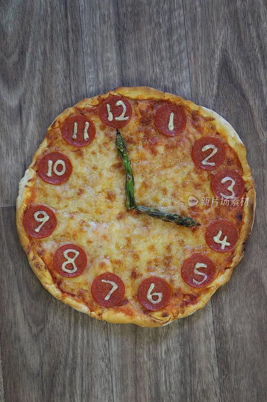 这是一个自制的披萨时钟，上面有意大利辣香肠片、马苏里拉奶酪和芦笋作为时钟指针，显示时间是16:00到4:00，这是意大利披萨餐厅为孩子们的生日聚会食物而制作的儿童披萨时钟