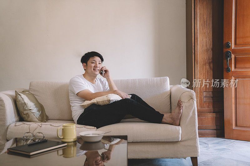 一位亚洲华人男性周末在客厅的沙发上听智能手机