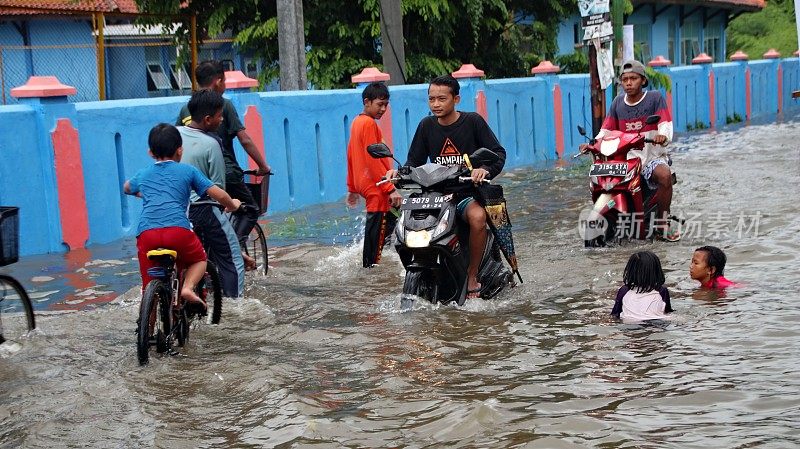 居民和学生在经过被洪水淹没的道路时