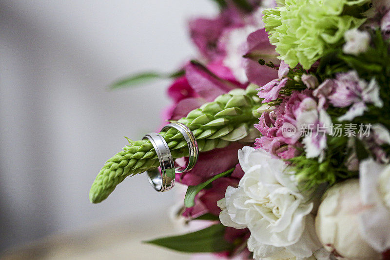 一对银色的结婚戒指挂在婚礼花束的一部分上