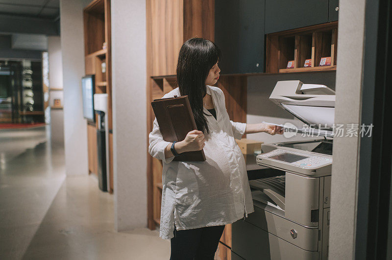 一位亚裔华裔孕妇在办公室用复印机复印文件