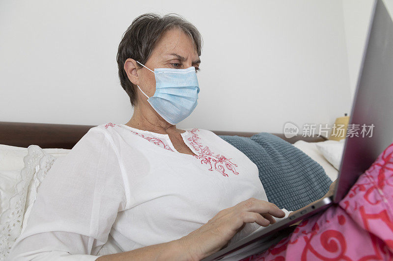 妇女生病在床上戴口罩使用笔记本电脑
