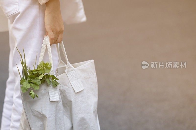 为了减少全球变暖，年轻女性早上在新鲜市场用可回收袋购买蔬菜。