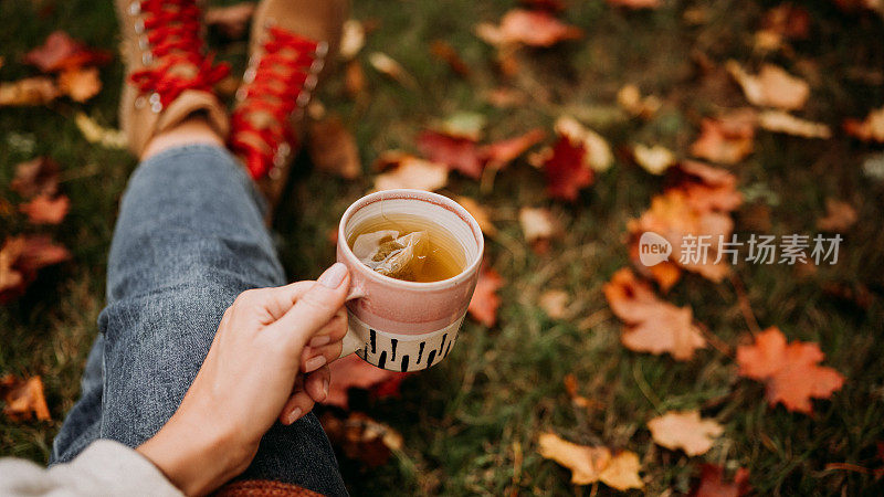 在户外喝茶的女人在秋天休闲装近陶瓷茶杯