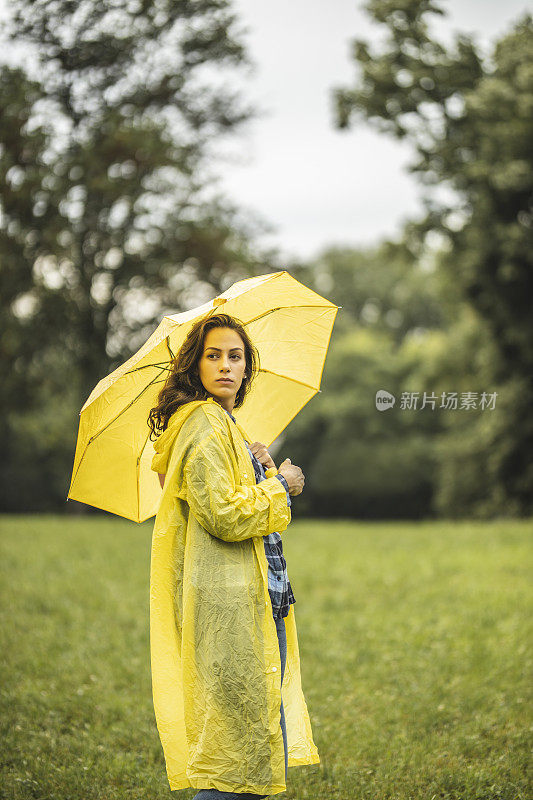 女人穿着雨衣，撑着雨伞，在雨天行走