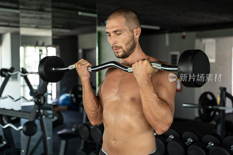 肌肉健美的帅哥在健身房用哑铃练二头肌。强壮的运动员有腹肌和二头肌。