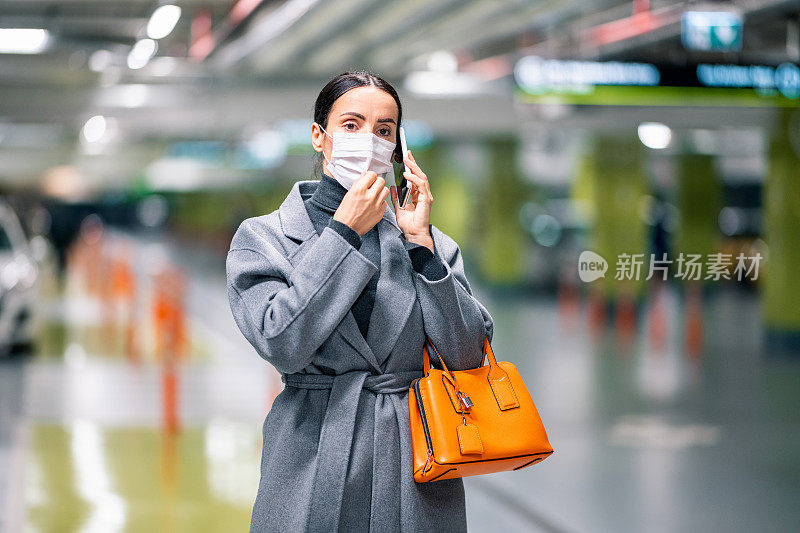 在新冠肺炎大流行期间，戴着防护口罩在停车场打电话上班的女性