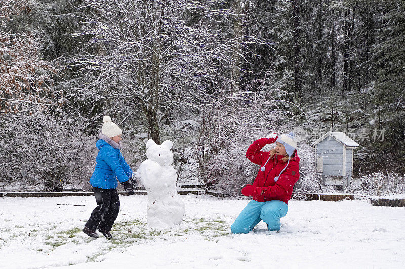 白种女孩带着一个孩子，一个5岁的女孩，玩和扔雪球。冬季与家人欢度周末。