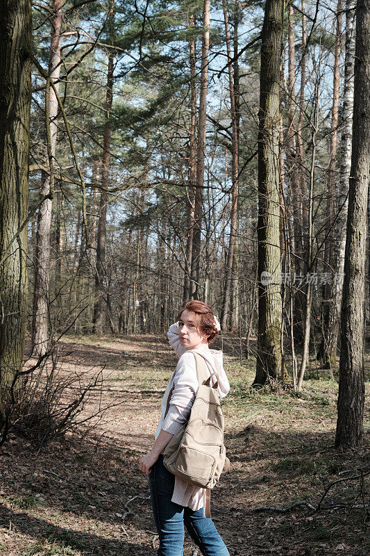 成熟的女人走在阳光明媚的森林里，站着环顾四周
