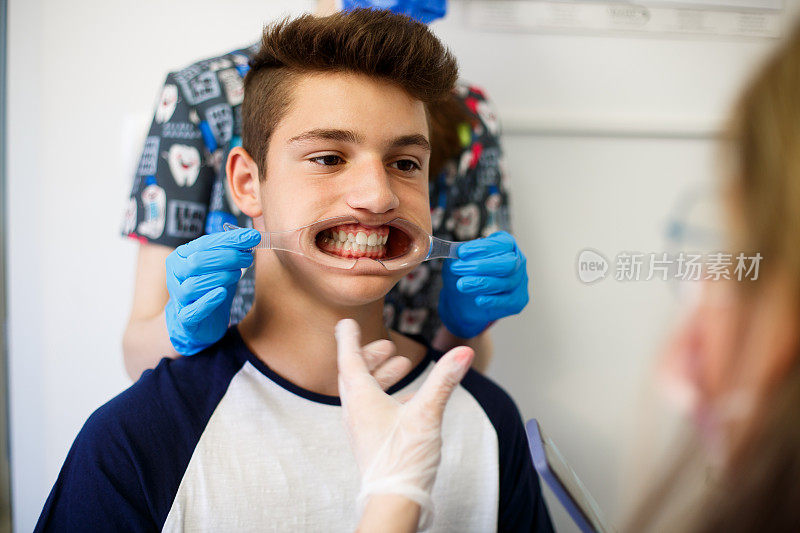 男孩坐着，牙医助手正在把脸颊拉钩插入他的嘴里。