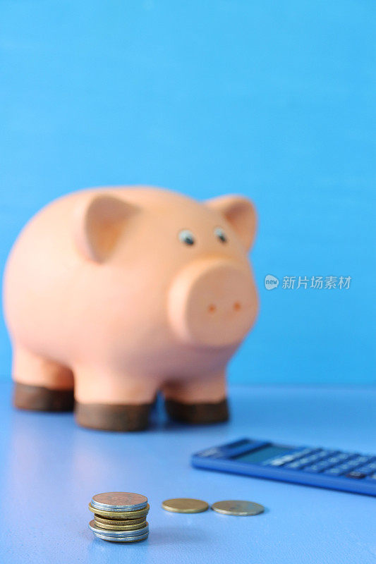 图片的储蓄罐坐在一个计算器和一堆硬币，蓝色背景，重点前景，抵押贷款，家庭财务和储蓄的概念