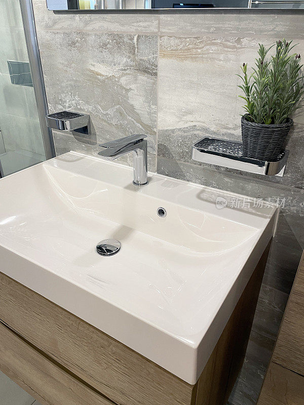 近景的现代浴室与铬，单一的杠杆整体搅拌机水龙头在白色，矩形陶瓷水槽梳妆台在墙镜下，天然石材墙瓷砖