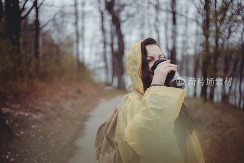 一个快乐的年轻女子在一个下雨天穿着一件黄色雨衣在树林里享受大自然。
