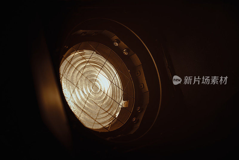 在黑暗的背景上，使用菲涅耳镜头的专业照明设备的特写。照片中的照明装置位于左下方，在右上方发光。