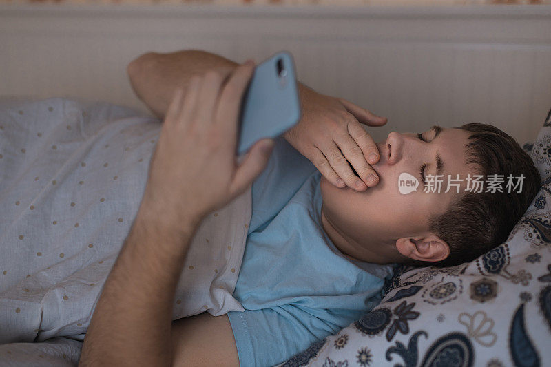 困倦的男子打着哈欠，用手捂住嘴。男人半夜醒来，在网上冲浪，不能入睡。社交媒体成瘾，手机依赖。