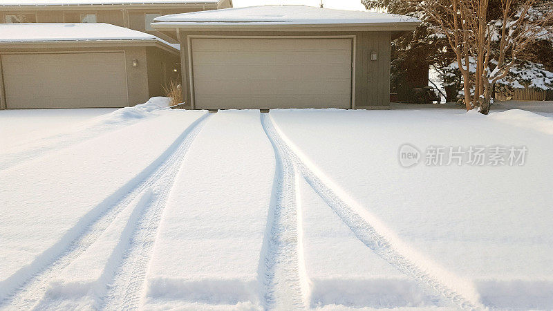 从住宅车库穿过原始积雪车道的汽车轮胎痕迹