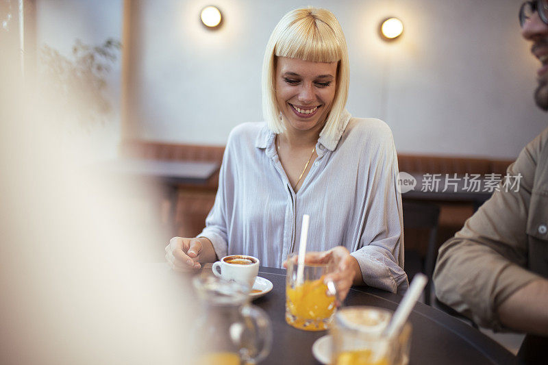 一个穿着白衬衫的女人坐在咖啡店里，和朋友们坐在一起，享受着闲逛和喝咖啡的乐趣。