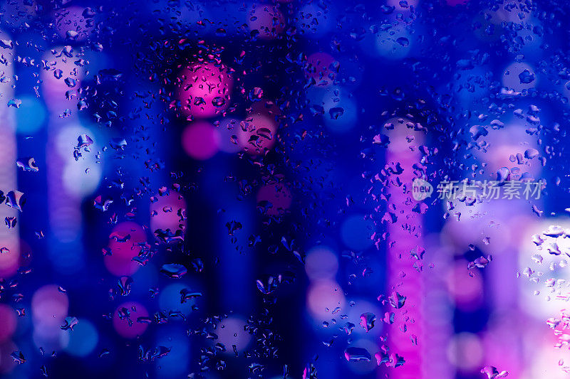 在霓虹灯的映衬下，雨滴凝结在窗玻璃上