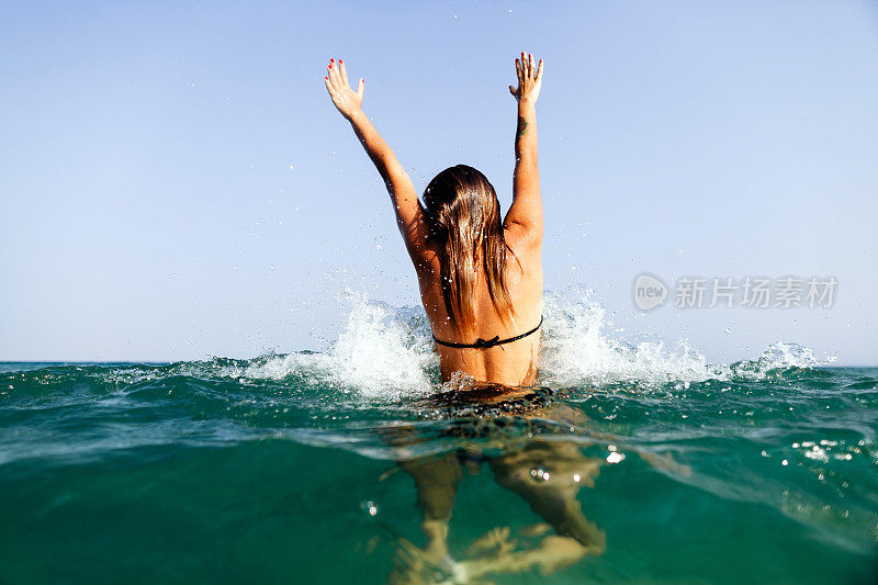 性感的女孩游泳海浪手向上飞溅的背影