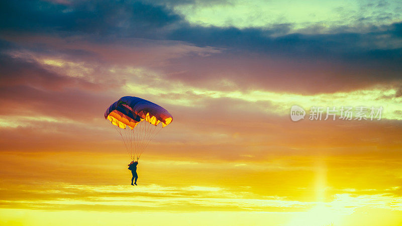 在阳光明媚的日落日出的天空中乘坐彩色降落伞的跳伞者
