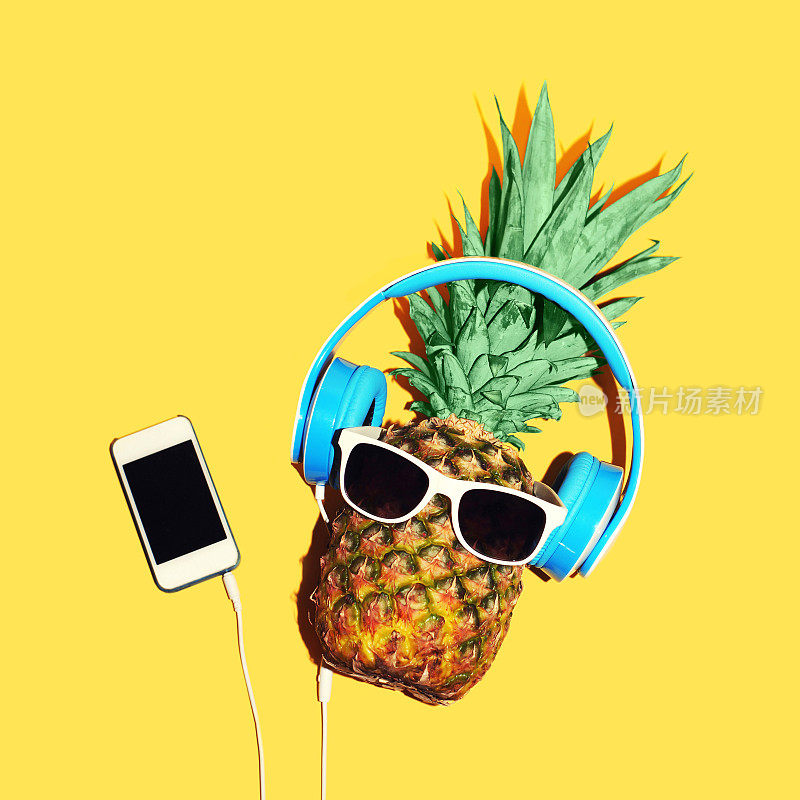 时尚菠萝戴着太阳镜和耳机用智能手机听音乐