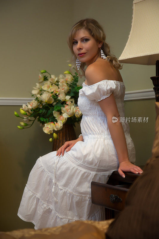 年轻女子穿着浪漫的白色连衣裙坐在卧室里