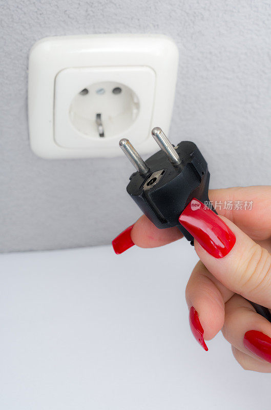 欧洲妇女将电源插头插入墙壁插座给电器供电