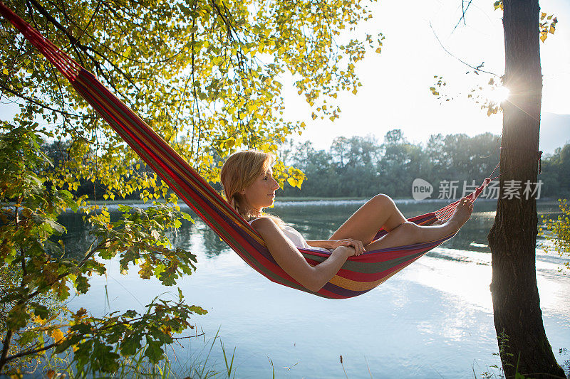 日落时分，女子在河边的吊床上休息。