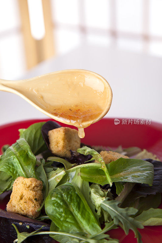 食物:绿色沙拉，调味汁从勺子倒在上面