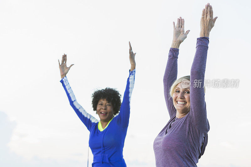 两个成熟的女人在海滩上锻炼，做瑜伽