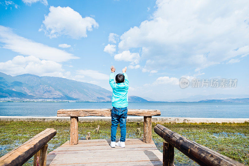 小中国男孩站在湖边举起双手