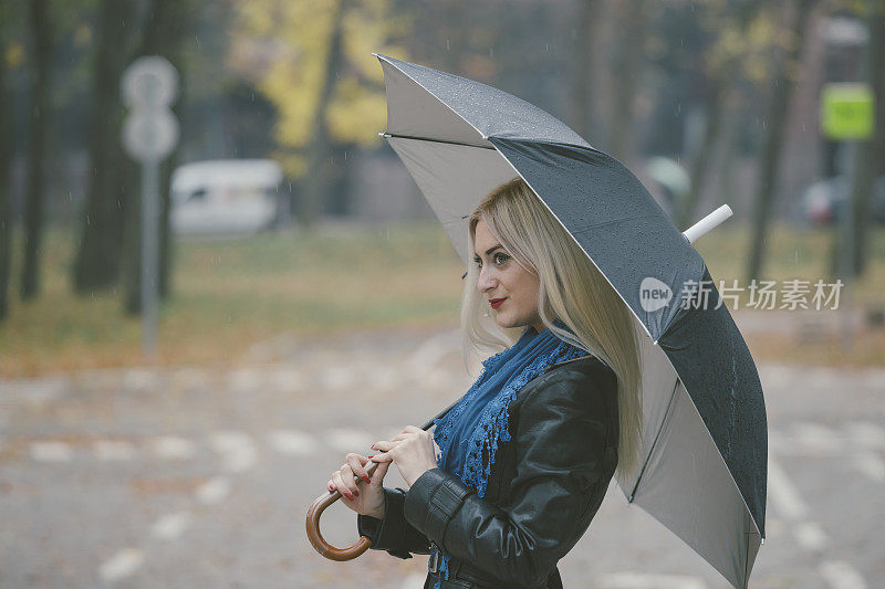 美丽的金发女孩带着伞在雨天路过