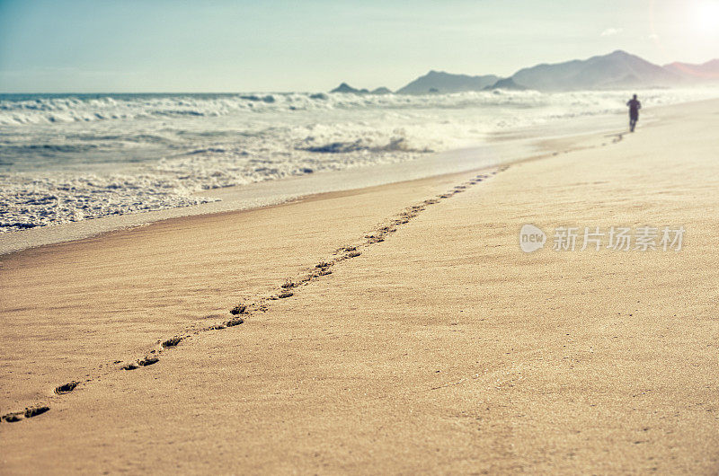 男人沿着海滩跑，留下了一长串脚印