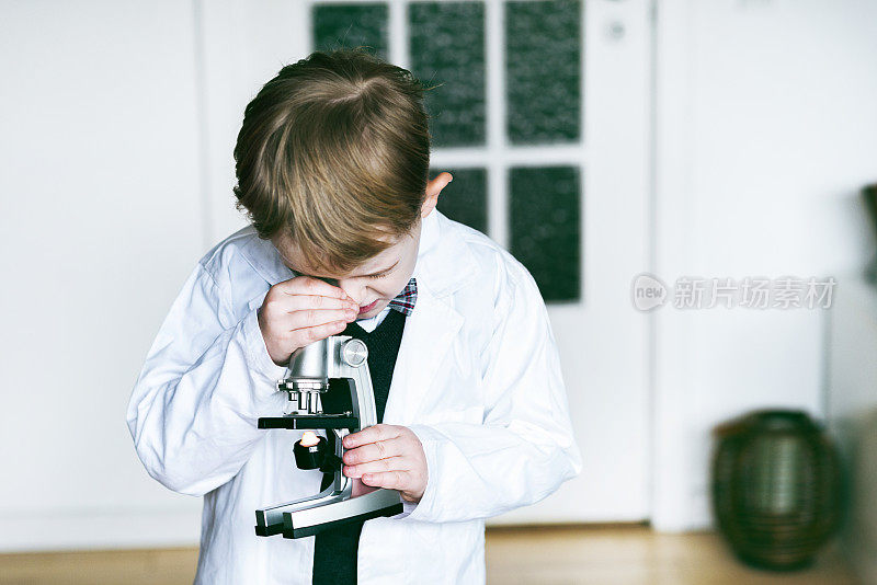 一个男生穿着实验服，通过显微镜检查一个物体