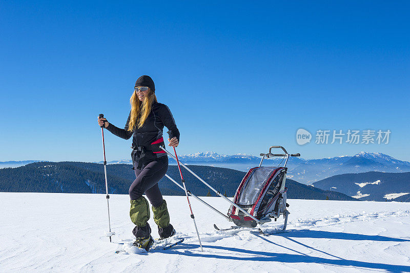 妈妈用雪鞋在雪景上拉着婴儿滑雪拖车