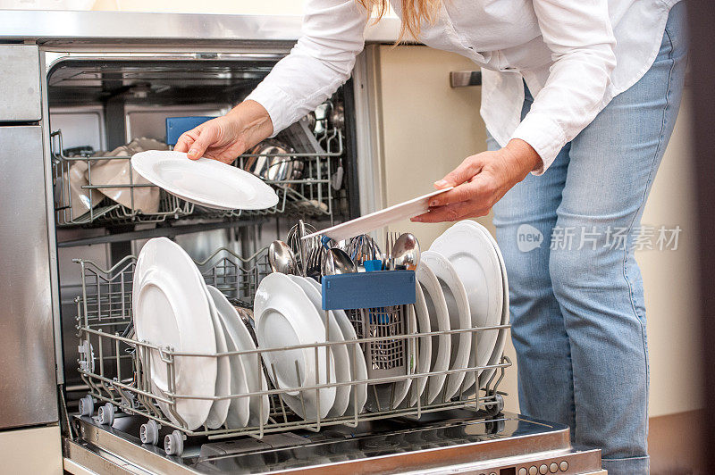 成年妇女在厨房里卸载洗碗机