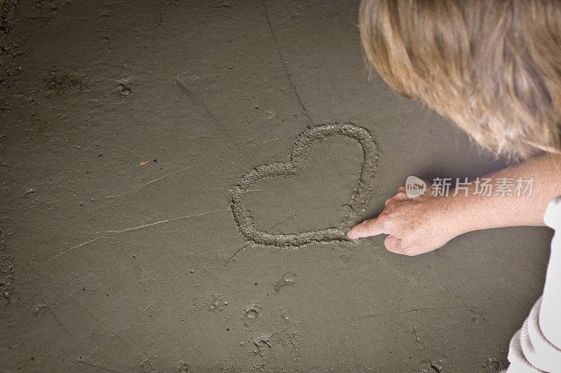 成熟的女人在湿水泥上画一颗心。