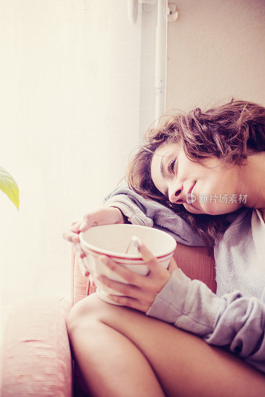 年轻女子在家里用茶碗做白日梦。