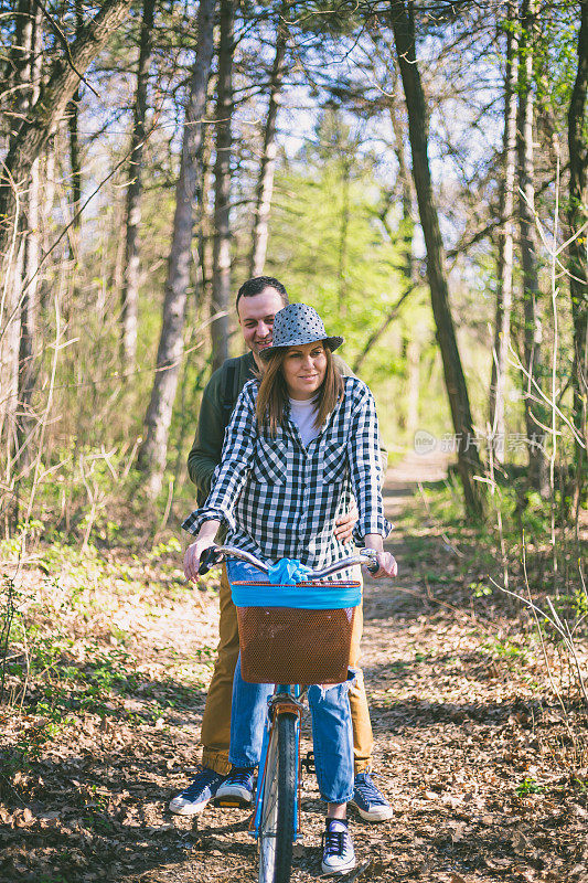 年轻夫妇在公园里玩得很开心。一对快乐的年轻夫妇在春天的一天在公园里骑自行车。